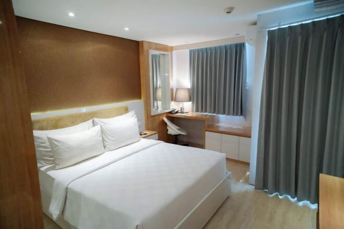 Una habitación de hotel con una cama grande, un escritorio, una silla y un ventanal con cortinas.