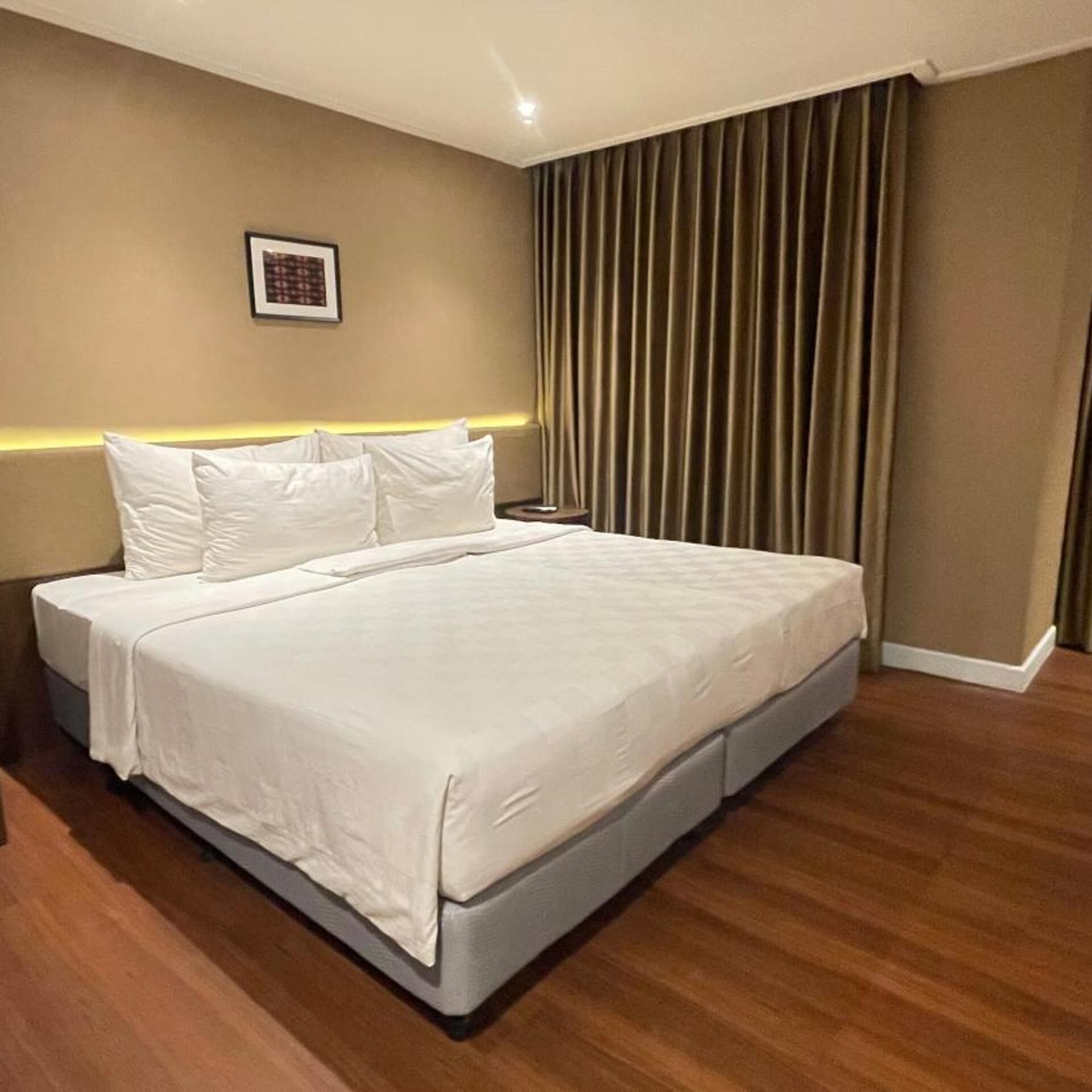 Un dormitorio moderno con una cama grande, cabecera con iluminación integrada y un cuadro enmarcado en la pared.
