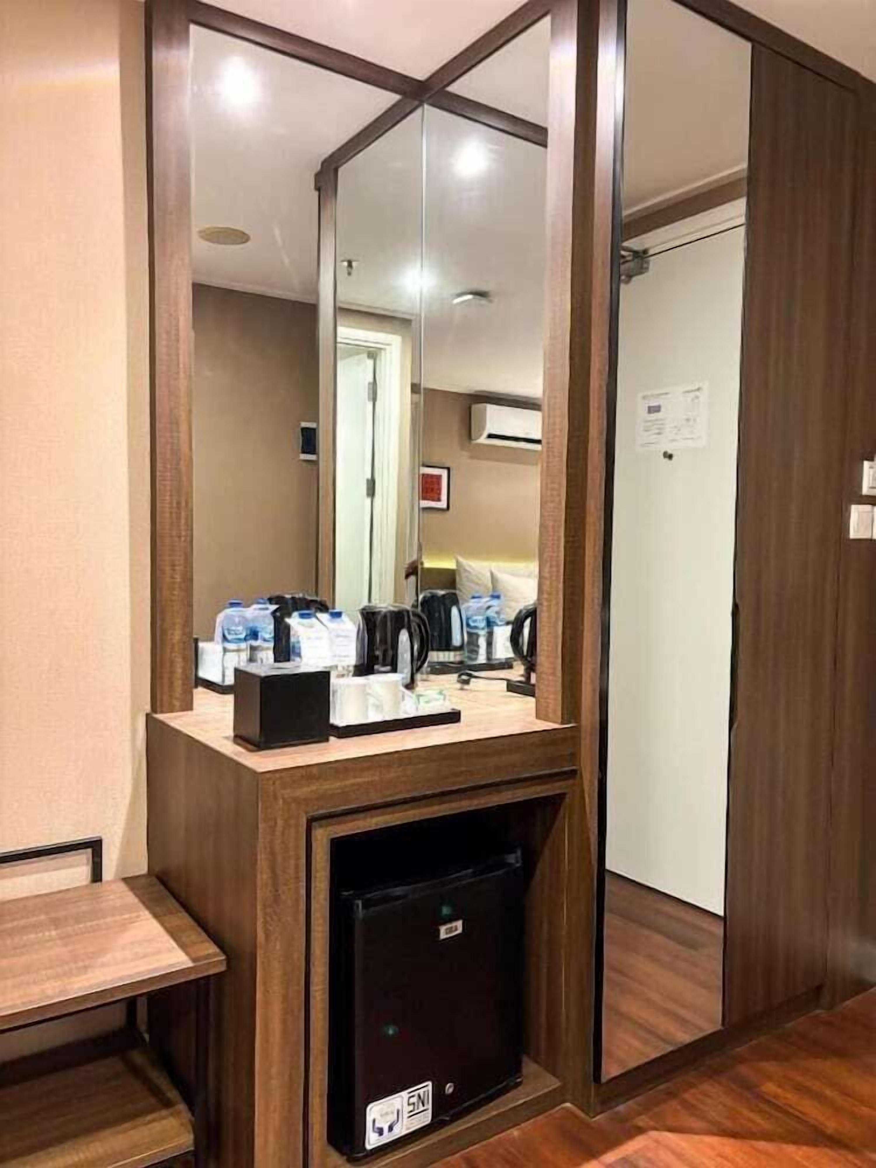 A hotel room with a wooden desk, a mirror, a mini-fridge, and a coffee station.