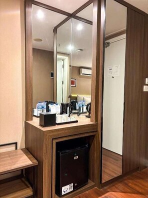 A hotel room with a wooden desk, a mirror, a mini-fridge, and a coffee station. - Swiss-Belcourt Serpong (SOUTH TANGERANG)