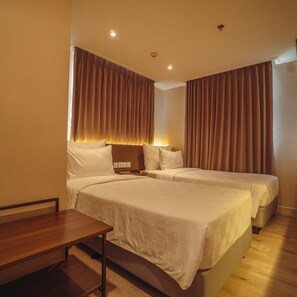 A hotel room with two beds, a wooden desk, and a headboard with integrated lighting. - Swiss-Belcourt Serpong (SOUTH TANGERANG)