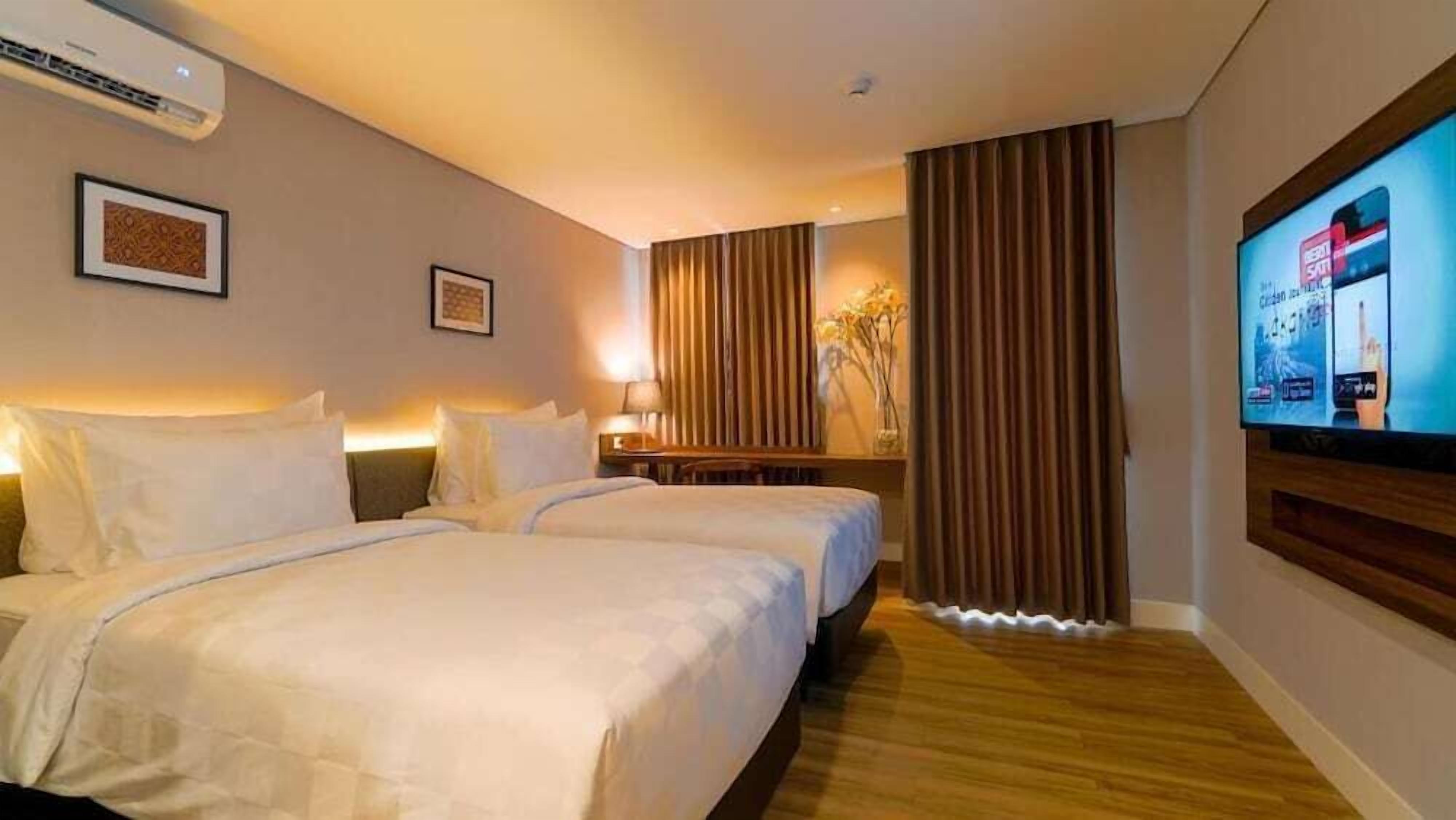 Habitación de hotel con dos camas, un escritorio, televisor y un ventanal con cortinas.