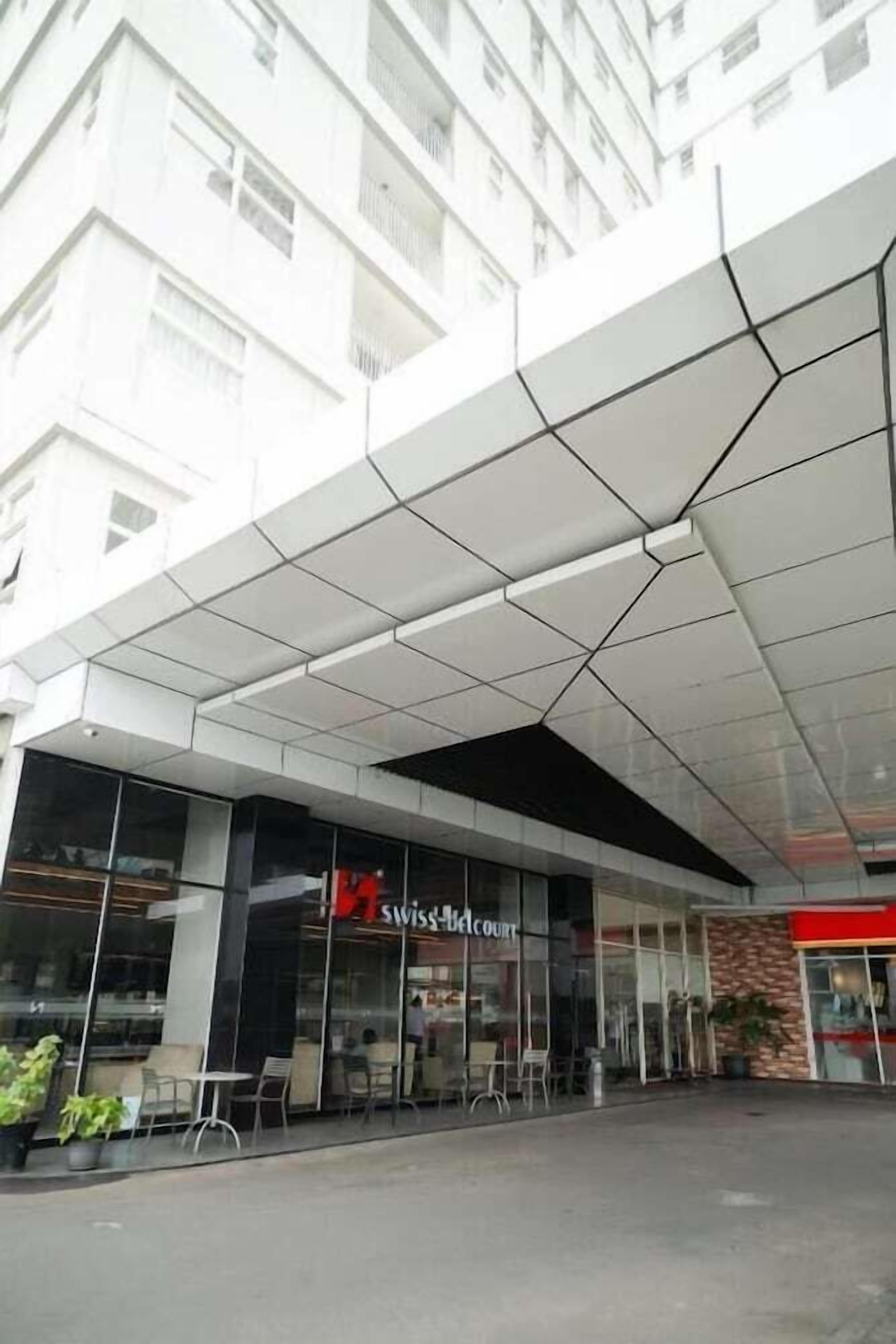 A modern building with a glass facade, a SwissBelCourt sign, and outdoor seating.