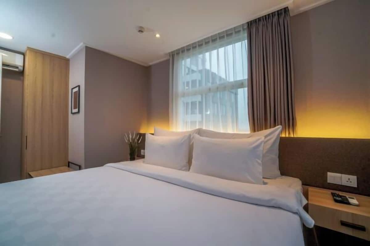 Habitación de hotel con una cama grande, una mesita de noche, cortinas en la ventana y un aire acondicionado instalado en la pared.