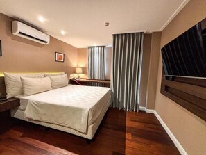 Habitación de hotel con cama, mesitas de noche, equipo de aire acondicionado, lámpara, cortinas y ventana.