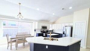 Una cocina moderna con una isla central, armarios blancos y una zona de comedor con sillas.