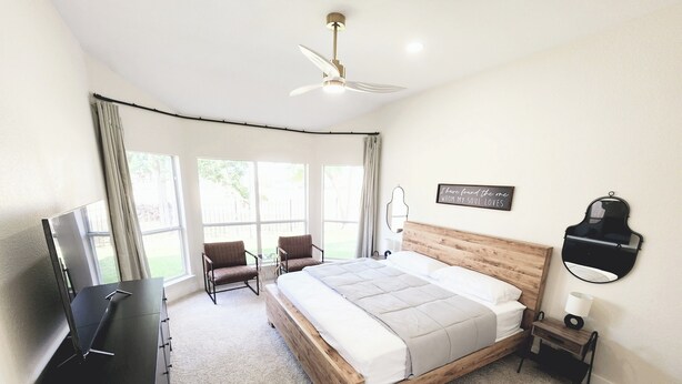 Un dormitorio con cama, televisor, ventilador de techo y ventana con cortinas.