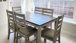 Un comedor con una mesa y sillas de madera, una araña y vistas a una cerca de madera a través de amplios ventanales.
