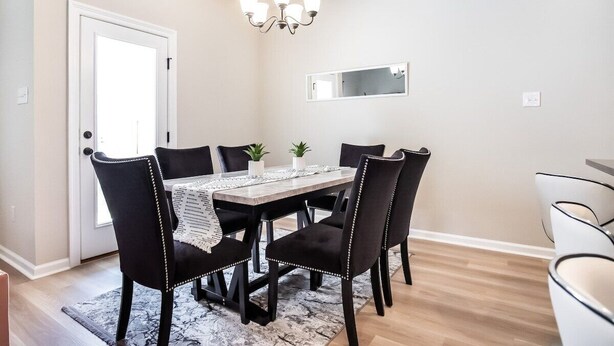 Un espace repas comprenant une table, des chaises, un lustre et un miroir au mur.