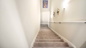 Un escalier recouvert de moquette, doté d’une rampe, avec des murs blancs et un tableau encadré accroché au mur.