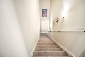A carpeted staircase with a handrail, white walls, and a framed picture on the wall.
