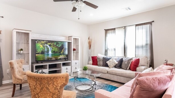 A modern living room with a flat-screen TV, a sofa, a chair, and a ceiling fan. - Bayou Bengal Royal Stay-n-Tailgate by LSU - BC1025 (Baton Rouge)