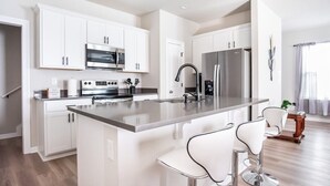 Une cuisine moderne avec des meubles blancs, des appareils en acier inoxydable et un îlot central doté de tabourets de bar.