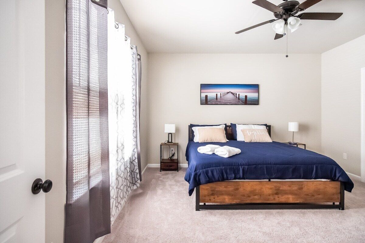 Una camera da letto con un letto, un ventilatore a soffitto, un comodino, una lampada e un quadro appeso al muro.