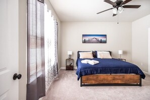 Une chambre à coucher avec un lit, un ventilateur de plafond, une table de chevet, une lampe et un tableau au mur.