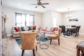 Un salon spacieux comprenant un canapé, des fauteuils, une table à manger et un ventilateur de plafond.