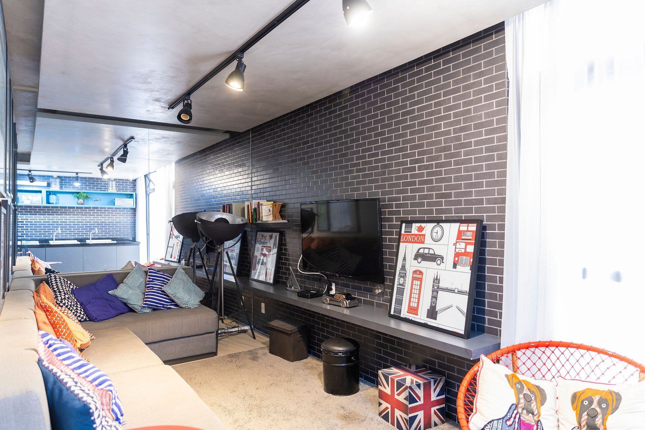 A modern living room with a grey sofa, a television, and a brick wall.