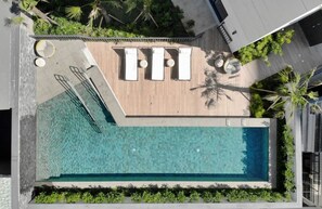 An aerial view of a rooftop swimming pool with three sun loungers, a wooden deck, and surrounding greenery. - Setin Downtown Genebra (São Paulo)