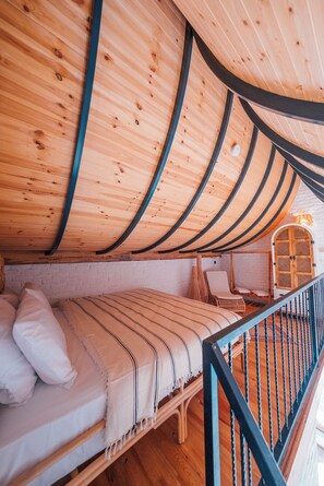 A cozy room with a curved wooden ceiling, a bed with a striped blanket, a chair, and a small table. - Feronia Suites (Kartepe)