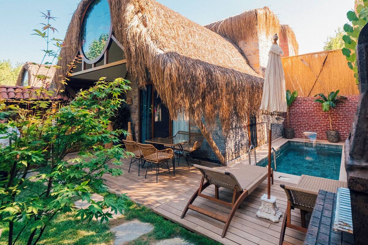 Uma casa com telhado de palha, piscina, área de estar externa e um deck de madeira.