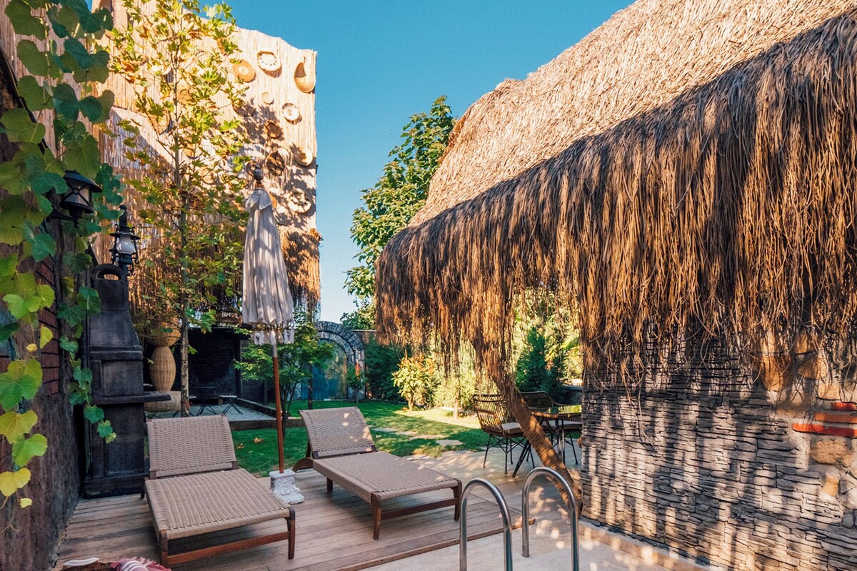 A pool area with lounge chairs, a hot tub, and a stone wall.