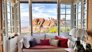 Una habitación con un sofá blanco, varias ventanas y vistas a edificios y al mar.