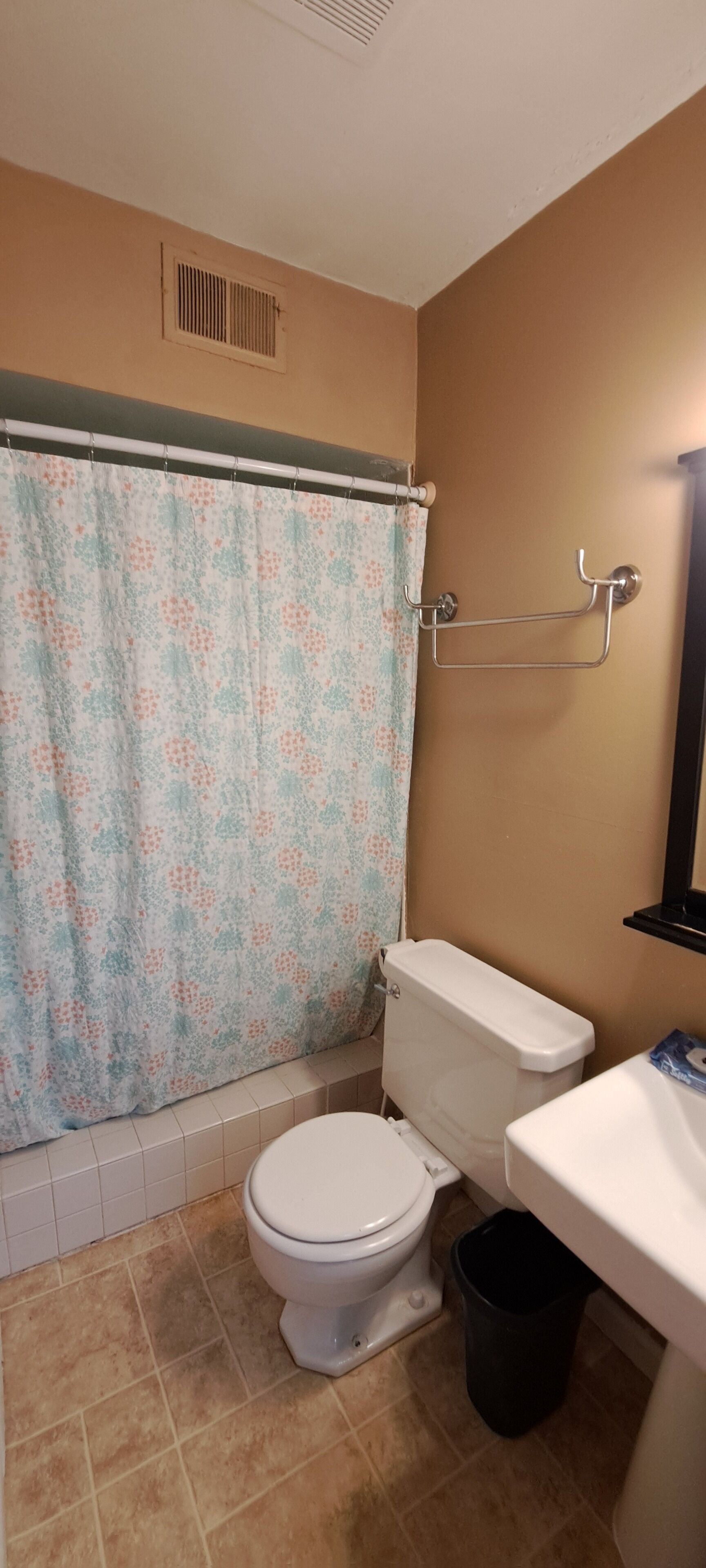A bathroom with a toilet, a shower curtain, a towel rack, and a sink.