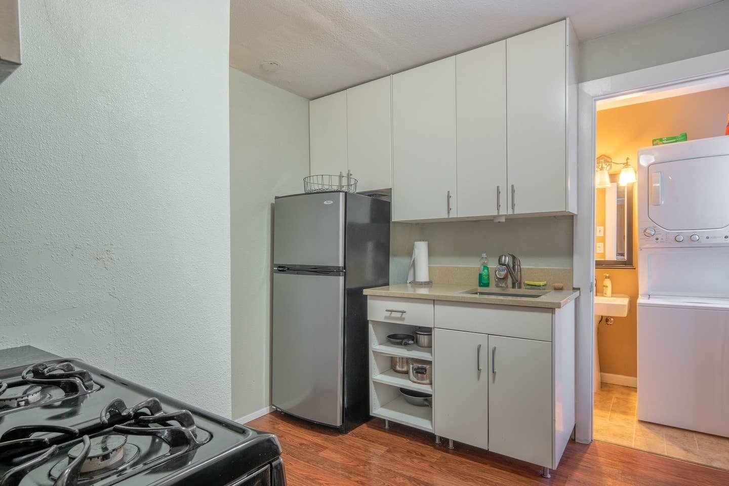 A compact kitchen with a gas stove, stainless steel refrigerator, white cabinets, and a sink.