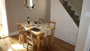 A dining area with a wooden table set for four, a bottle of wine, and a mirror on the wall. - 2 bedroomed cottage in Hythe, Kent, close to amenities and beach. Dogs welcome. (Hythe)