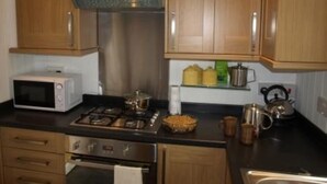A kitchen with wooden cabinets, a microwave, a stove, and a kettle on the counter. - 2 bedroomed cottage in Hythe, Kent, close to amenities and beach. Dogs welcome. (Hythe)