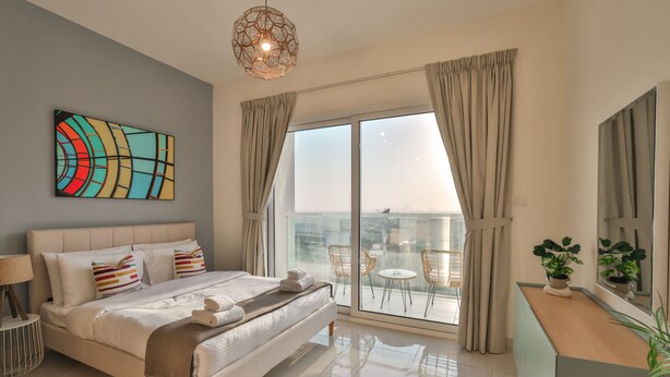 A modern hotel room with a large bed, a city view balcony, and a contemporary art piece on the wall.