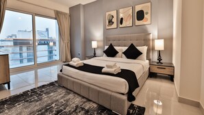 A modern hotel room with a large bed, two bedside tables, a nightstand, a large window with curtains, and artwork on the wall.