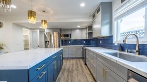 A modern kitchen with blue cabinets, stainless steel appliances, and a large island.