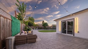 A patio with a wicker sofa, a trash can, and string lights.