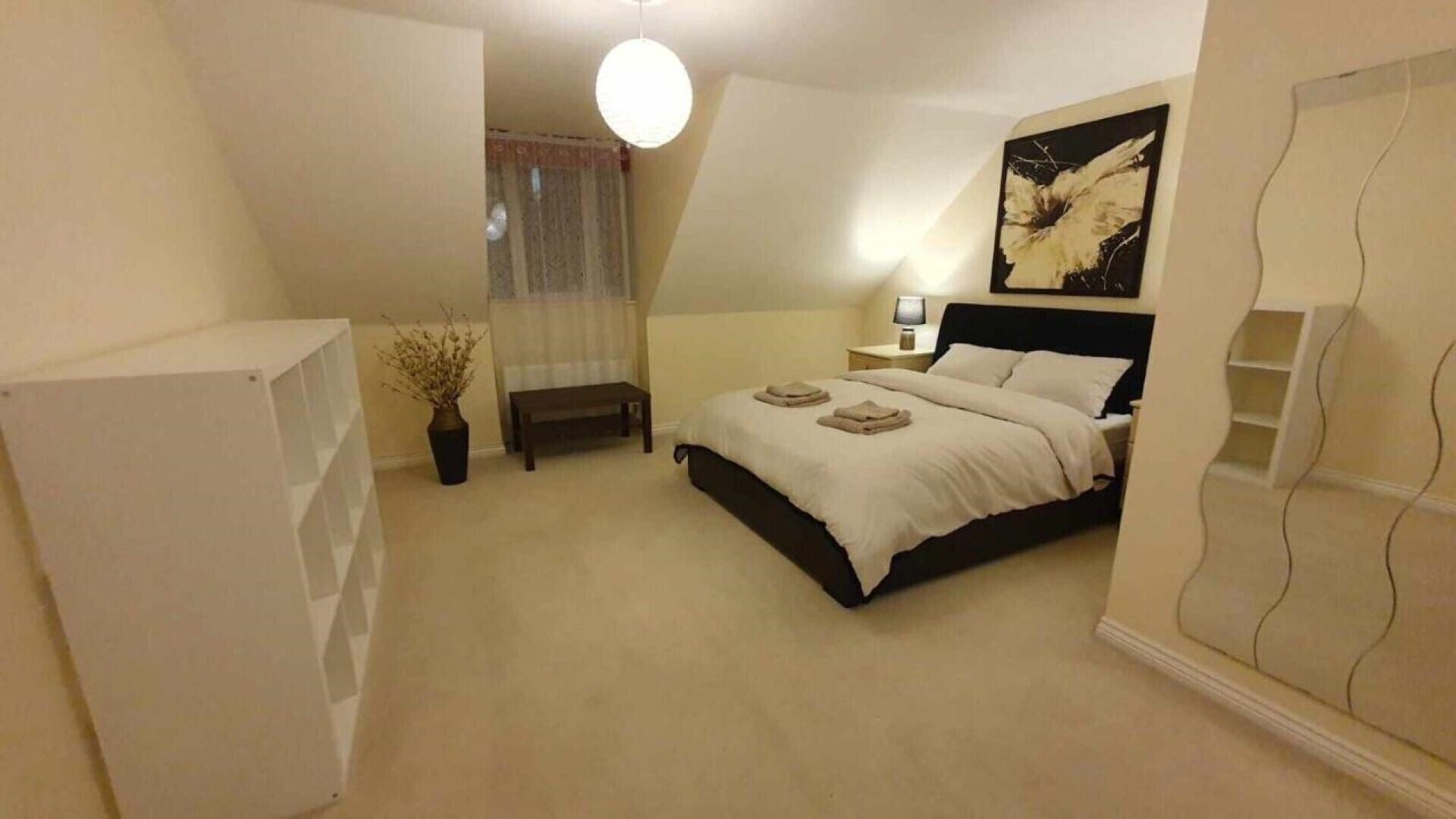 Een slaapkamer met een bed, nachtkastje, lamp en een schilderij aan de muur.