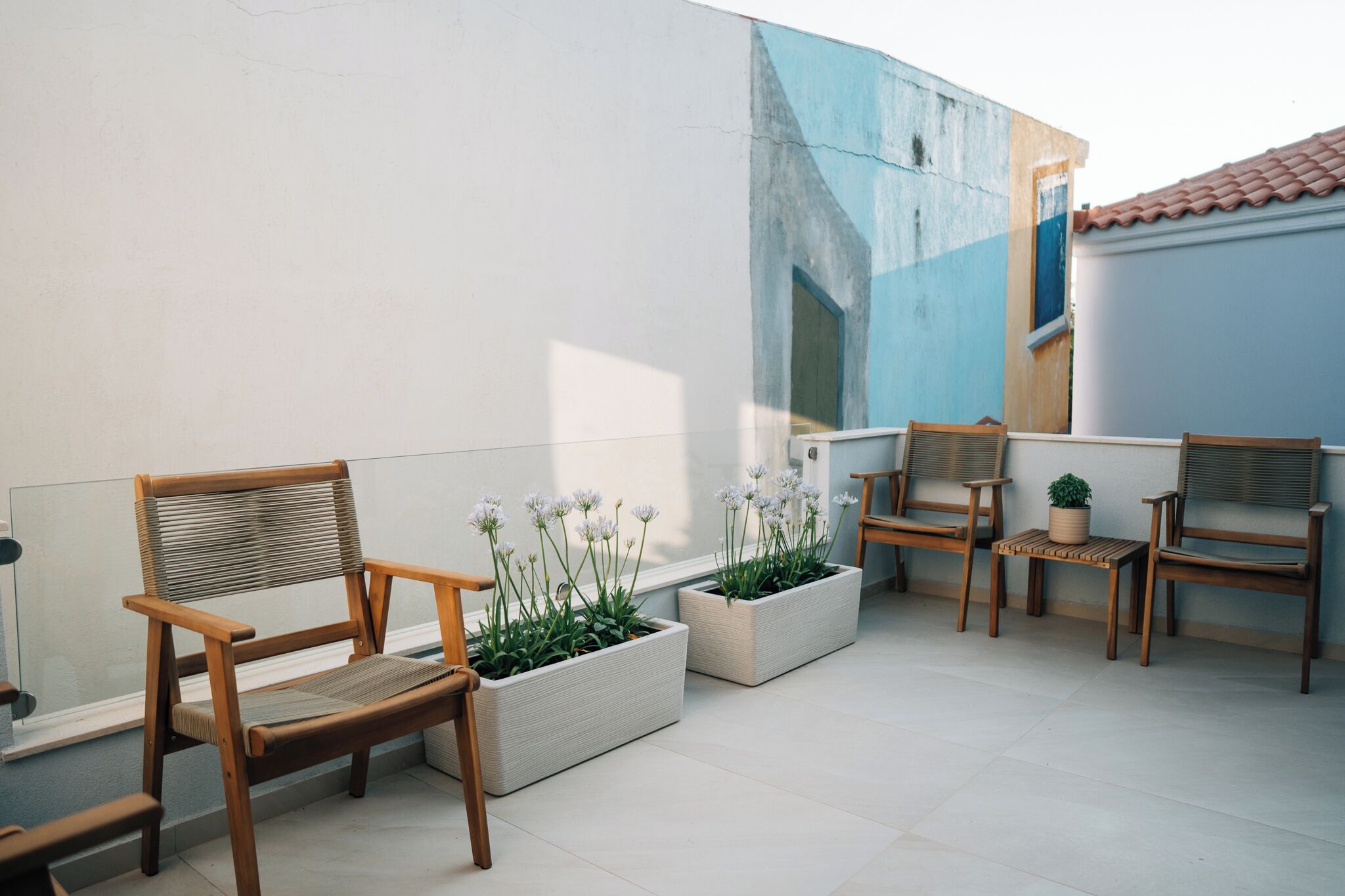 A patio with wooden chairs and planters with flowers.