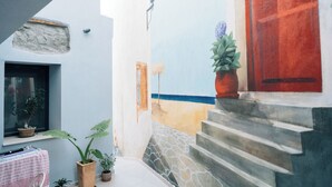 A narrow courtyard with a stone staircase, potted plants, and a red door.