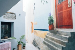 Un patio estrecho con una escalera de piedra, plantas en macetas y una puerta roja.