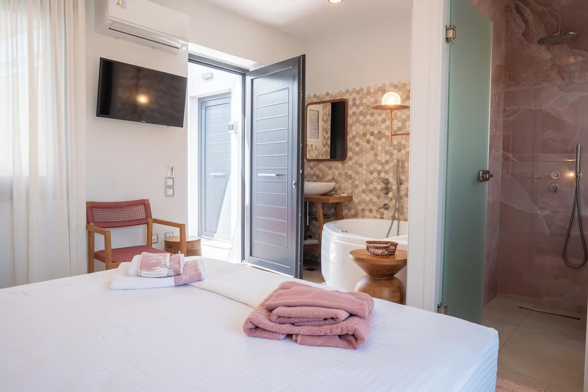 A hotel room with a bed, a TV, a bathroom with a shower, and a chair.