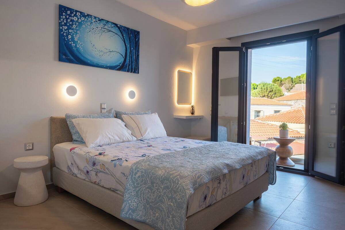 A bedroom with a bed, bedside table, and a view of the outside.