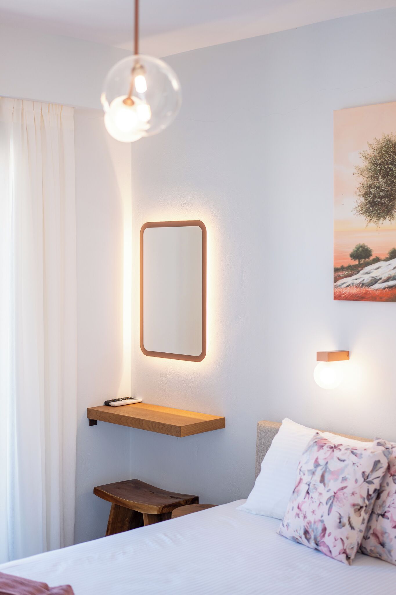 A bedroom with a bed, a bedside table, a hanging light fixture, a wall-mounted mirror, and a painting.