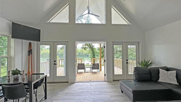 Amplio salón con techo alto, ventanas grandes y vista a una terraza con muebles de exterior.