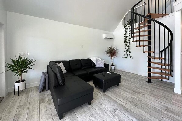 A modern living room with a black sectional sofa, a black ottoman, and a spiral staircase with a black railing.