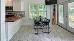 Una cocina moderna con armarios blancos, encimera de madera y un comedor con mesa y sillas de vidrio.