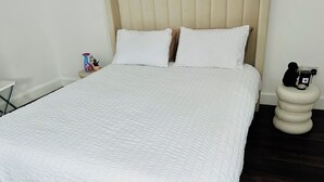 A neatly made bed with a white quilt, a headboard, and a bedside table with a lamp and a bottle.