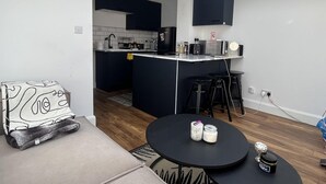 A compact living space with a kitchenette, a round dining table, and a sofa with a patterned throw.