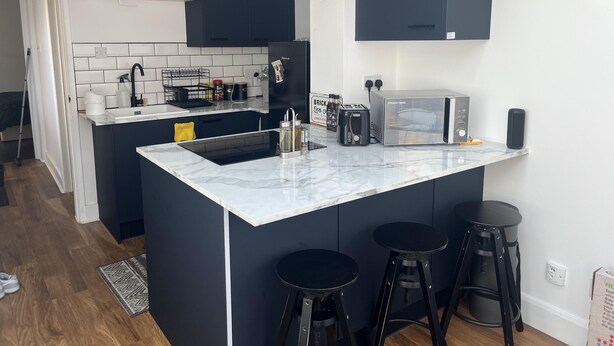 A modern kitchen with a central island, black bar stools, a microwave, and a toaster.