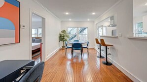 Une chambre d’hôtel moderne avec un plancher en bois, un coin repas avec des chaises bleues, une grande fenêtre et un escalier en arrière-plan.