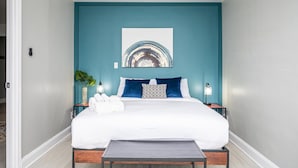 Une chambre à coucher comprenant un lit, un ventilateur de plafond, une œuvre d’art accrochée au mur, des tables de chevet et une table de nuit.