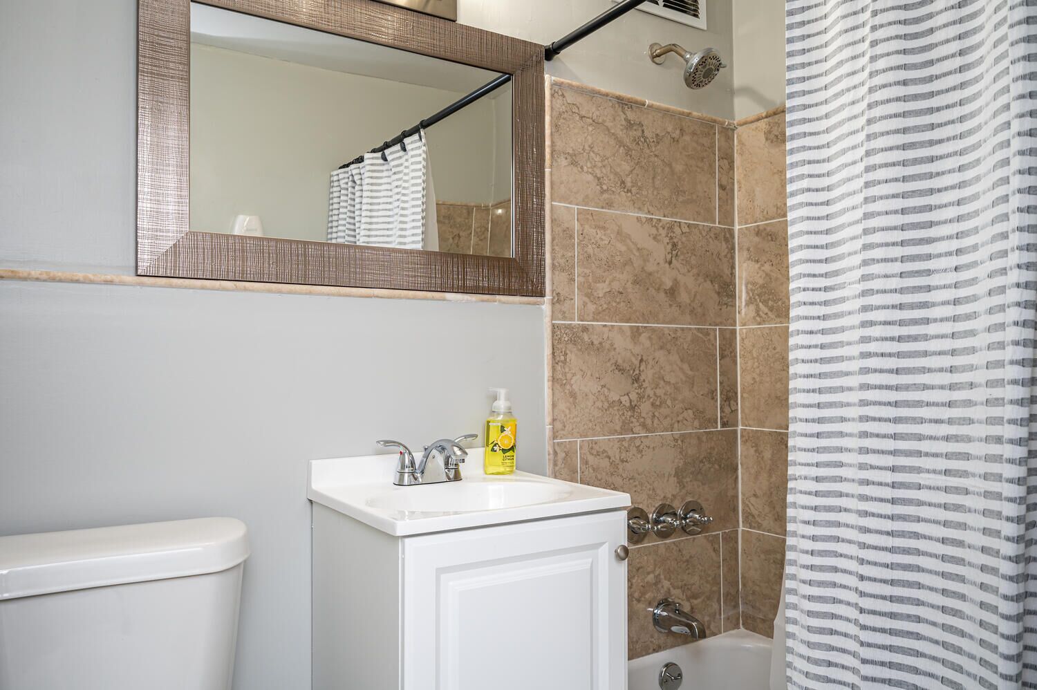 A bathroom with a white sink, a mirror, a shower with a striped curtain, and a toilet.
